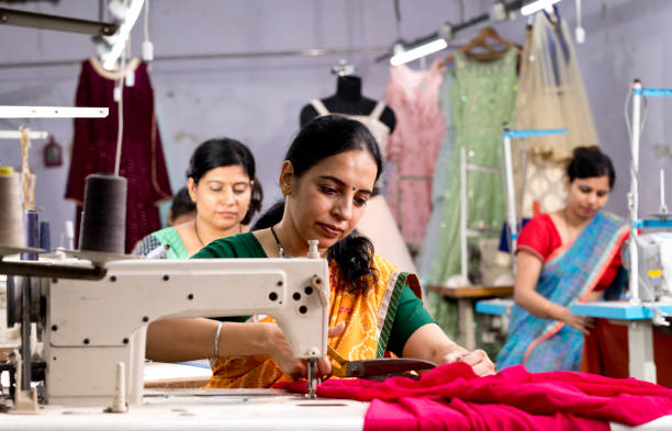 Female dressmaker cutting dress fabric on production line with sewing machine